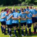 Spielerinnen stehen im Kreis. Zwei Spielerinnen feiern zusammen.