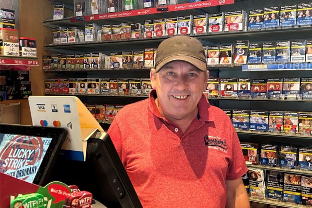 Michael Dorawa steht in seinem Kiosk. Hinter ihm ist ein großes Regal mit Zigaretten zu sehen.