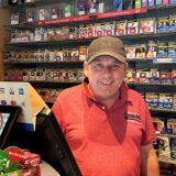 Michael Dorawa steht in seinem Kiosk. Hinter ihm ist ein großes Regal mit Zigaretten zu sehen.