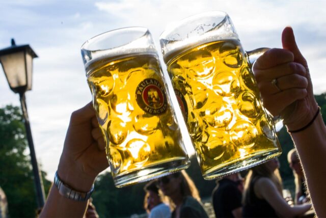 Zwei Menschen stoßen in einem Biergarten mit Bierkrügen an.