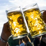 Zwei Menschen stoßen in einem Biergarten mit Bierkrügen an.