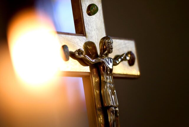 Holzkreuz mit goldener Jesusfigur im Kerzenschein