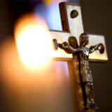 Holzkreuz mit goldener Jesusfigur im Kerzenschein