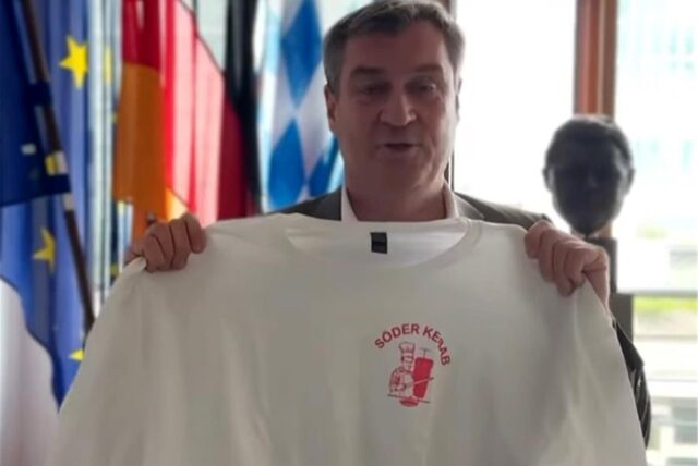 Bayerns Ministerpräsident Markus Söder hält ein T-shirt mit dem Aufdruck «Söder Kebab» in die Kamera.