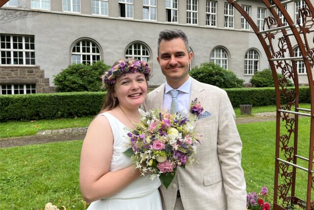 Marina und Julian Boneberger stehen frisch verheiratet vor dem Bogen am Rathaus in Schwerte.