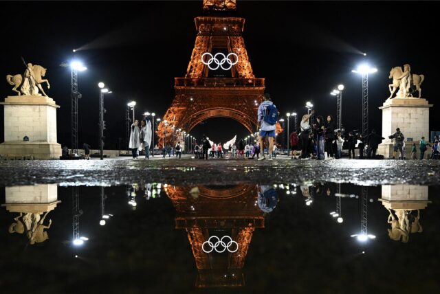Der Pariser Eifelturm geschmückt für Olympia, spiegelt sich in einer Regenpfütze.