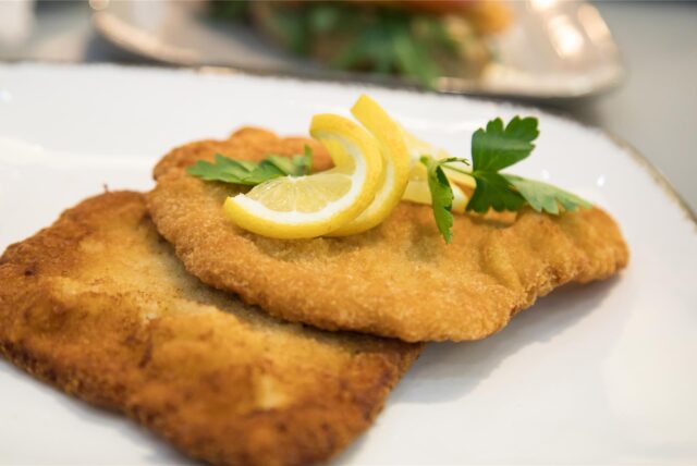 Zwei Schnitzel liegen mit Zitronenscheiben und Petersilie auf einem Teller.