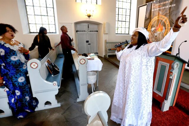 Eine Frau im weißen Gewand leitet afrikanischen Gottesdienst in der Lutherkirche.