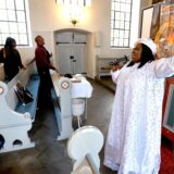 Eine Frau im weißen Gewand leitet afrikanischen Gottesdienst in der Lutherkirche.