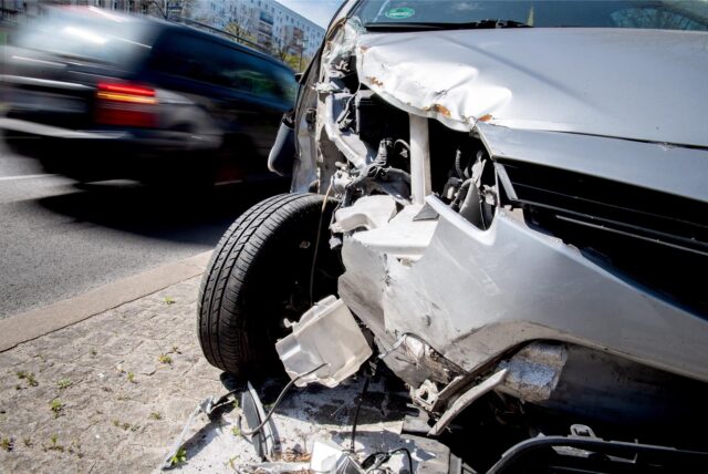 Ein beschädigtes Auto steht an am Straßenrand, ein anderes Auto fährt weg.