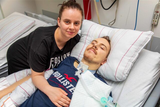 Lars Baranski liegt in einem Krankenbett. Er wird über einen Schlauch in seiner Luftröhre beatmet. Seine Frau Chantal Baranski beugt sich zu ihm herunter.