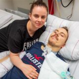Lars Baranski liegt in einem Krankenbett. Er wird über einen Schlauch in seiner Luftröhre beatmet. Seine Frau Chantal Baranski beugt sich zu ihm herunter.