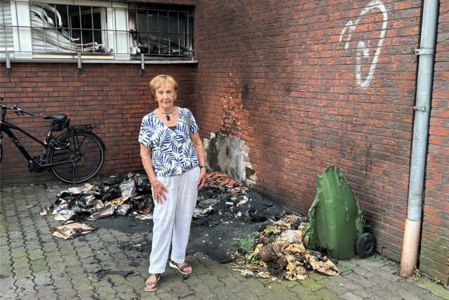 Hausbewohnerin Edith Brix vor den Resten der verbrannten Mülltonnen an einem Wohn- und Geschäftshaus an der Kämerstraßé