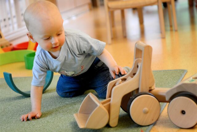 Ein Kleinkind spielt in der Kindertagesstätte mit einem Bagger aus Holz.