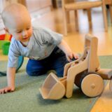 Ein Kleinkind spielt in der Kindertagesstätte mit einem Bagger aus Holz.