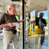 Ein Mann steht am Montag (5.8.) mit einem Päckchen vor der geschlossenen Postfiliale in Unna-Königsborn
