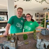 Bastian Dulczeski und Jenny Karras stehen im Laden „Two Tale Games“ in Schwerte-Ergste vor einem Tisch mit Miniatur-Häusern.