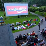 Kino-Karren im Elsebad in Schwerte-Ergste: Menschen haben es sich gemütlich gemacht und erwarten den Film. Die Leinwand steht auf der Liegewiese.