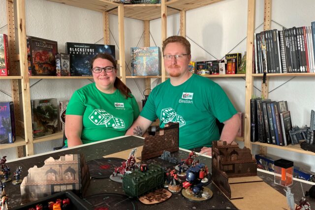 Jenny Karras und Bastian Dulczeski sitzen in ihrem Laden „Two Tale Games“ in Schwerte an einem Tisch mit Warhammer-Figuren.