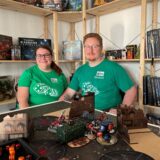 Jenny Karras und Bastian Dulczeski sitzen in ihrem Laden „Two Tale Games“ in Schwerte an einem Tisch mit Warhammer-Figuren.
