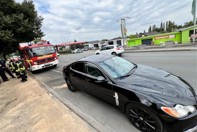 Die Feuerwehr wurde zu einem vermeintlichen Fahrzeugbrand an die Werner Straße in Bergkamen gerufen. Ein Wagen der Feuerwehr steht an der Hauptstraße hinter einem schwarzen Jaguar. Am Straßenrand mehrere Feuerwehrleute.