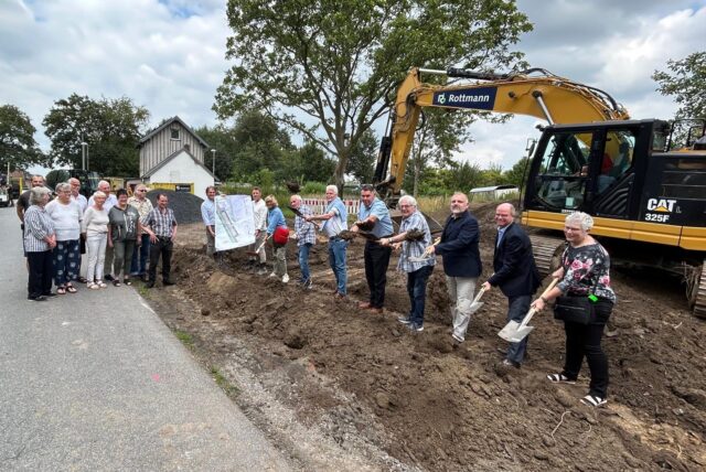 An der Lünerner Bahnhofstraße in Unna stehen einige Personen neben oder in einer Baustelle. Im Hintergrund steht ein Bagger