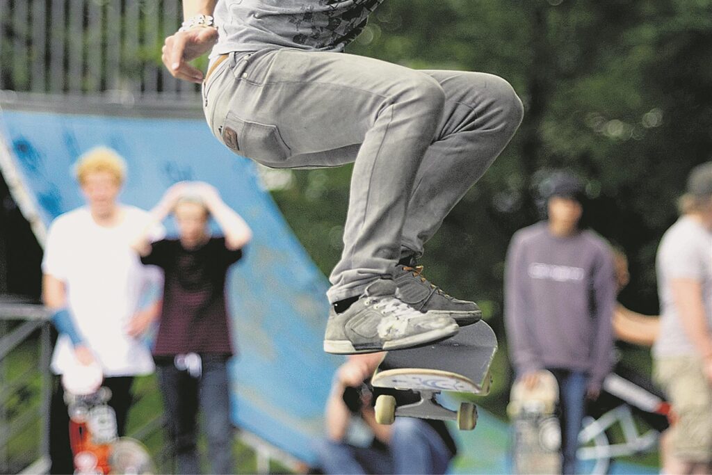 Ein Junge springt mit einem Skateboard an dem Fuß.