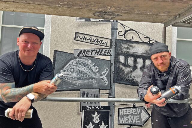 Zwei Graffiti-Künstler stehen auf einem Gerüst und haben ein Kunstwerk an eine Hauswand in Kamens Innenstadt gesprüht.