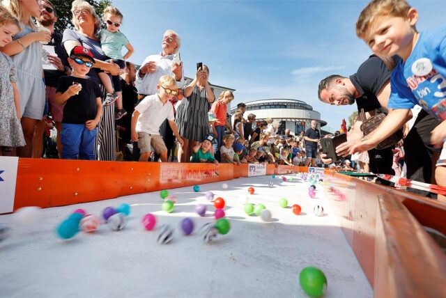Beim Bällerennen 2023 in Unna stehen zahlreiche Kinder und Erwachsene an der Strecke. Über eine Bahn rollen zahlreiche bunte Bälle.