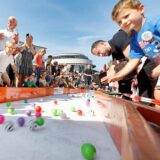 Beim Bällerennen 2023 in Unna stehen zahlreiche Kinder und Erwachsene an der Strecke. Über eine Bahn rollen zahlreiche bunte Bälle.