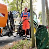 Christian Gramsch von der Stadt Unna befüllt einen Gießsack an einem Baum mit Wasser. Neben ihm steht ein Fahrzeug mit einem orangen Tank