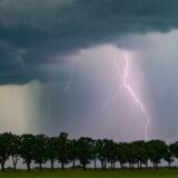 Ein Gewitter wurde über einer Baumreihe fotografiert.