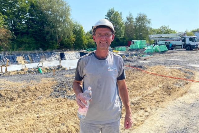 Bauarbeiter Mario Fricke steht auf einer Baustelle mit einer Flasche Wasser in der Hand