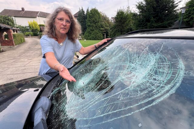 Eine Frau zeigt die eingeschlagene Frontscheibe ihres Autos