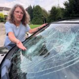Eine Frau zeigt die eingeschlagene Frontscheibe ihres Autos