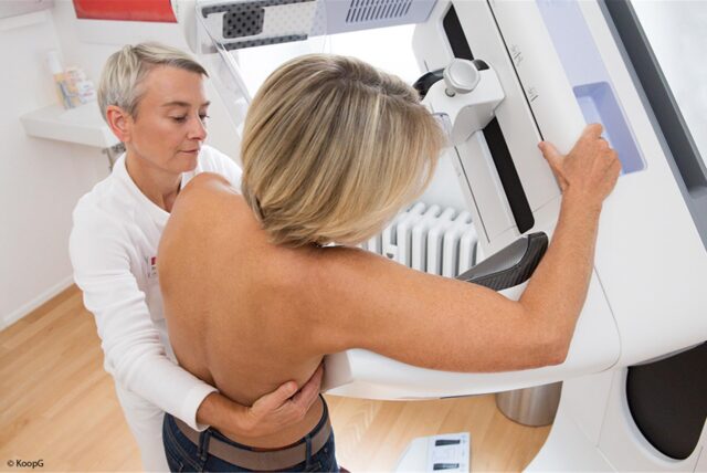 Eine Patientin steht an einem Mammographie-Gerät, während eine Ärztin ihren Arm um sie gelegt hat.
