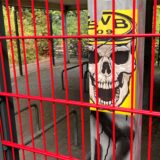 Am Bahnhof Unna-Königsborn ist ein BVB-Aufkleber mit einem Totenkopf durch einen Metallzaun hindurch zu erkennen.
