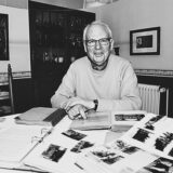 Dr. Gerhard Kummer sitzt an einem Tisch mit vielen Fotos und Fotoalben und lächelt in die Kamera