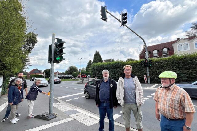 An der Hammer Straße in Unna stehen mehrere Personen an einer Fußgängerampel. Auf der Straße neben ihnen fahren Autos vorbei.
