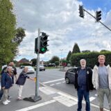 An der Hammer Straße in Unna stehen mehrere Personen an einer Fußgängerampel. Auf der Straße neben ihnen fahren Autos vorbei.