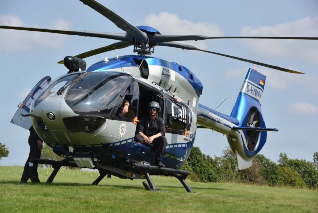 Der Hubschrauber Hummel 5 der Polizeifliegerstaffel NRW steht auf einer Wiese. Ein Polizist sitzt an der geöffneten Schiebetür.