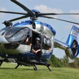 Der Hubschrauber Hummel 5 der Polizeifliegerstaffel NRW steht auf einer Wiese. Ein Polizist sitzt an der geöffneten Schiebetür.