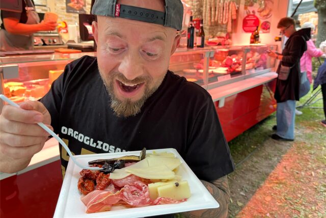 Ein Mann zeigt einen Teller mit Fleisch und Käse auf dem Streetfood-Markt in Schwerte.