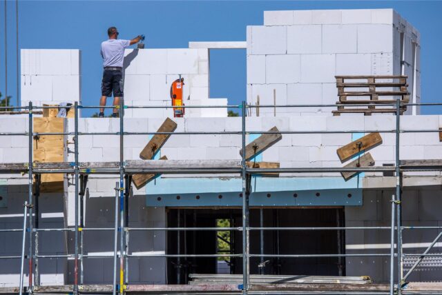 Ein Maurer arbeitet auf einer Baustelle, auf der ein großes Haus entsteht