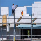 Ein Maurer arbeitet auf einer Baustelle, auf der ein großes Haus entsteht