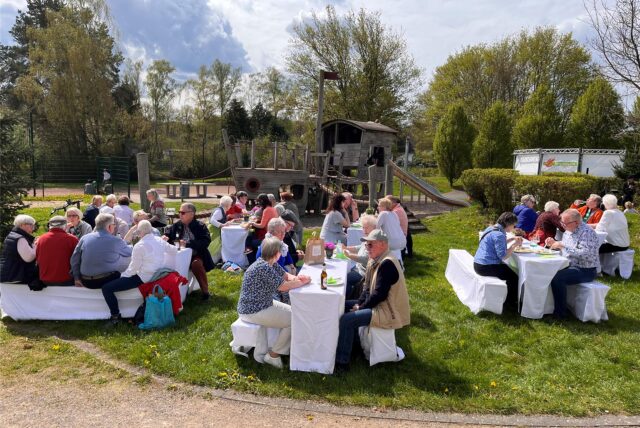 Mehrere Menschen sitzen an verschiedenen Tischen auf einem Spielplatz.