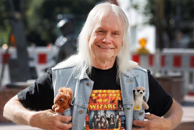 Reiner Barth mit auffälligem Look in Jeans-Weste, aus deren Taschen Stofftiere gucken.