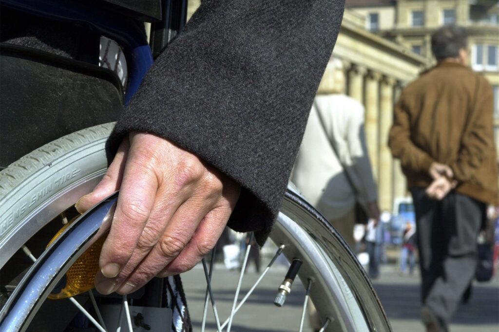 Die Hand eines Rollstuhlfahrers liegt auf dem Rad Die Hand eines Rollstuhlfahrers liegt auf dem Rad