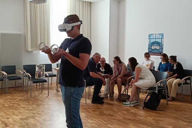 Gruppe beim Museumsforum im Gespräch, Mann mit VR-Brille vorne.