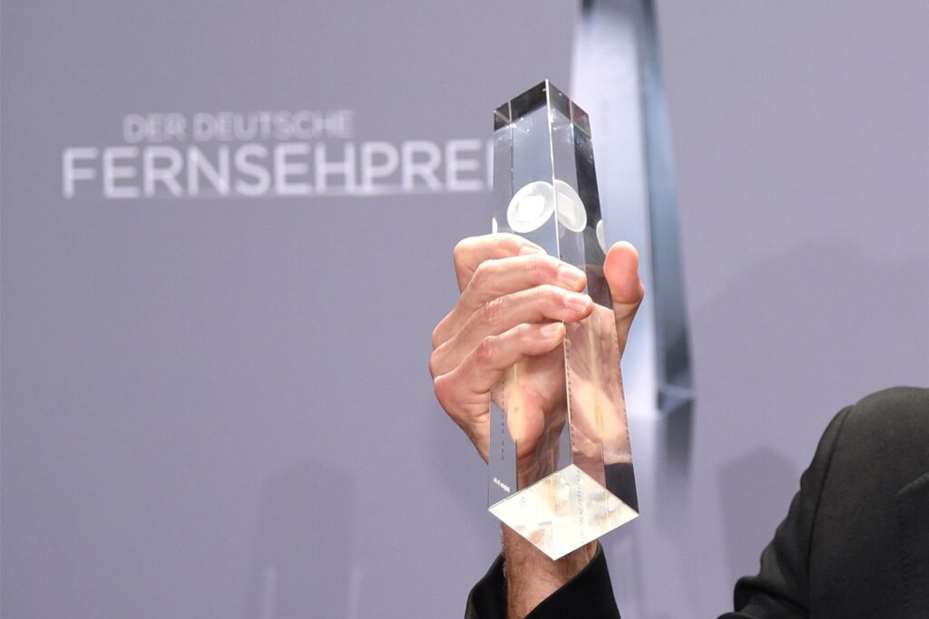 Eine Person hält die Trophäe des Deutschen Fernsehpreises.